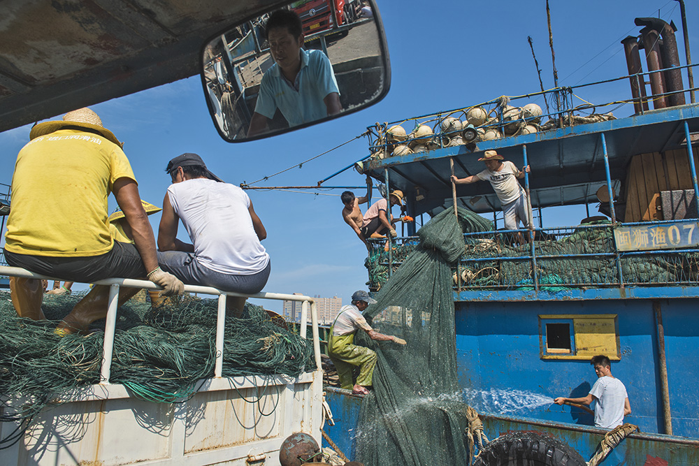 《渔港映像》组照22船上的鱼工清洗渔网,岸上的把清洗好的装车
