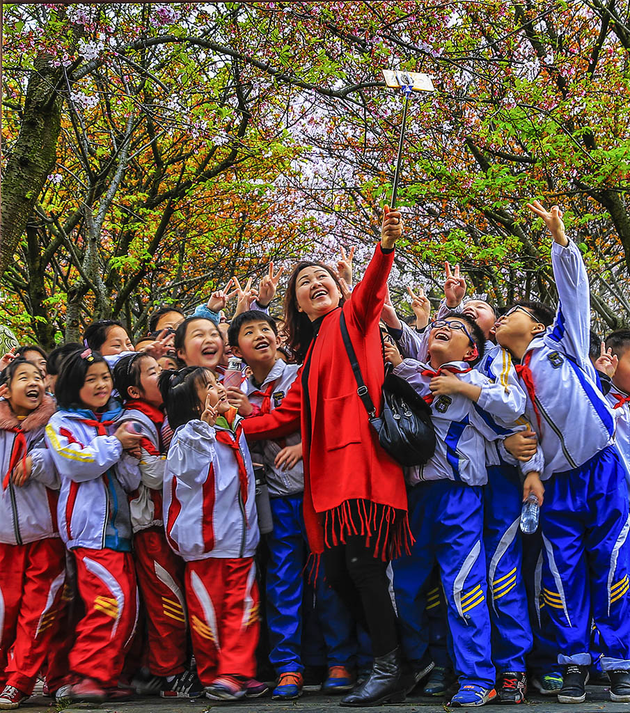 在江西九江甘棠公园,一群学生正围着老师在盛开的花下开心的合影留念