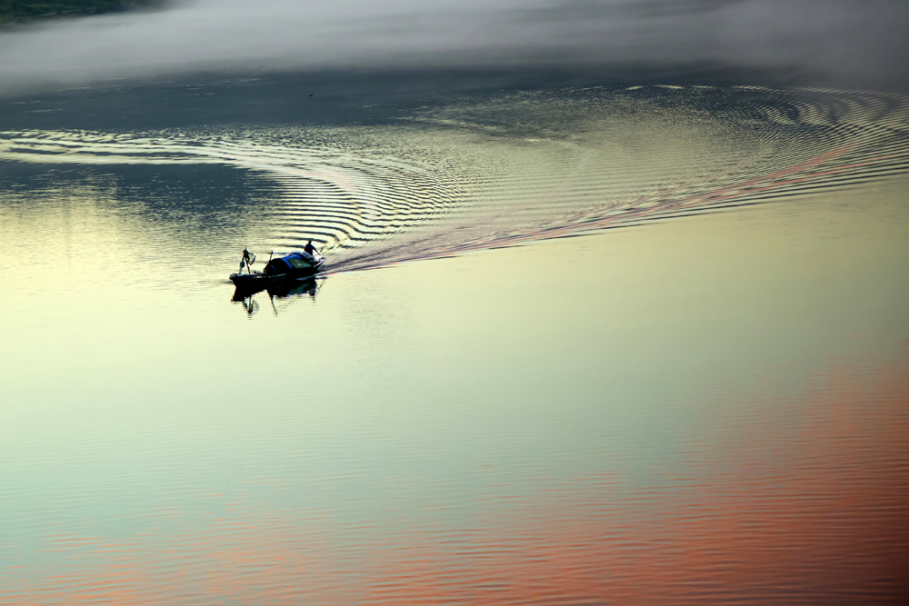 早晨阳光初照在江面上,一条渔船在江驰过的光景美景. .