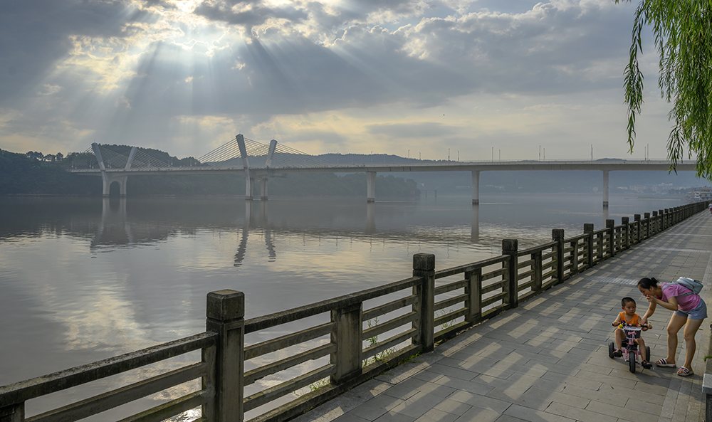 摄于合川滨江路,图片呈现出万丈光芒照射下的滨江路休闲步道上,年轻的