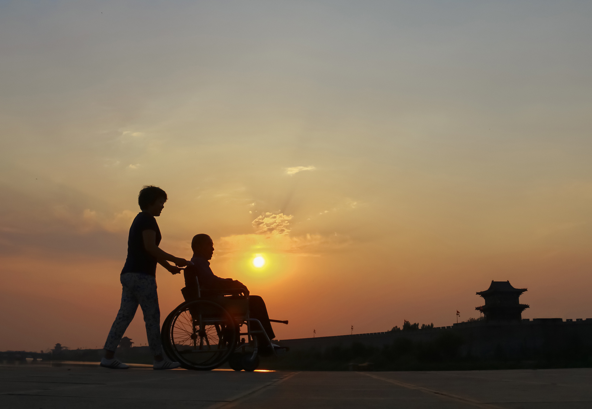夕阳下,一位女儿推着轮椅上的父亲游览广府古城.
