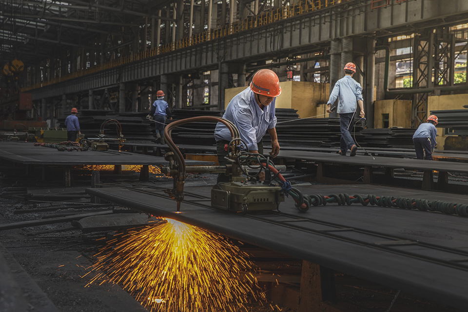 中板厂车间内,工人们正忙将钢板按尺寸切割,一时钢花四溅,谱写一曲曲